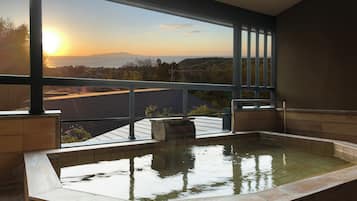 A hot tub with a view of a sunset over a hilly landscape.