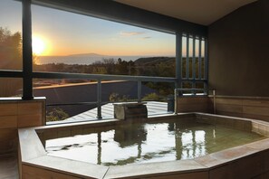 Un bain à remous offrant une vue sur un coucher de soleil se déclinant sur un paysage vallonné.