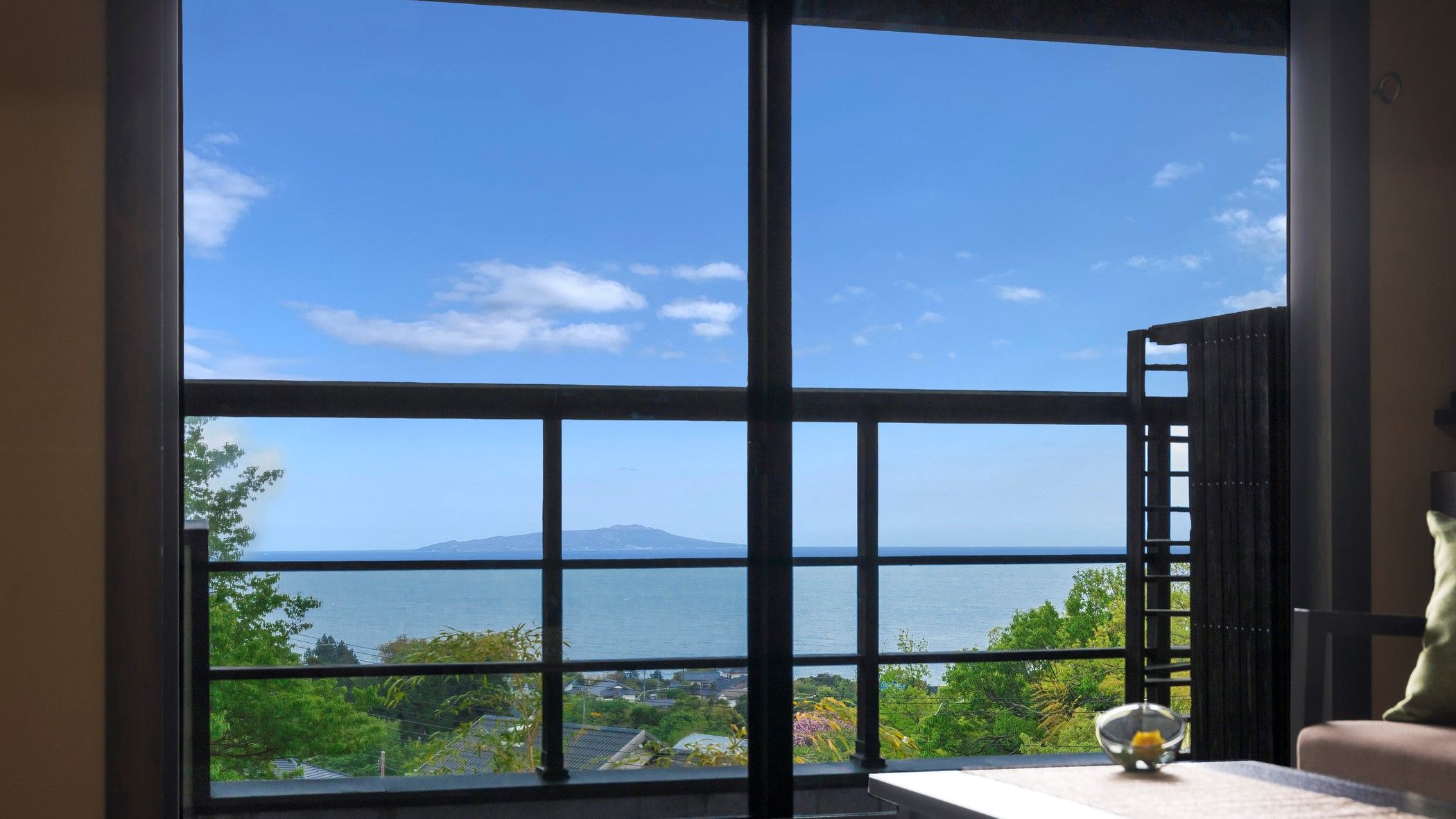 A room with large windows offering a view of a body of water and a distant mountain.