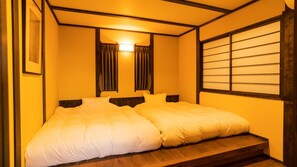 A double bed with a wooden headboard, a bedside table, and a window with horizontal blinds. - Gourmet Inn Izunohana (Ito)