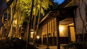 Un bâtiment traditionnel à ossature en bois, entouré de bambous et éclairé par un éclairage chaleureux.