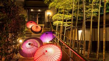 A night scene with a staircase, bamboo plants, and illuminated umbrellas.