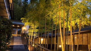 A building with a staircase leading to a covered area, surrounded by bamboo trees. - Gourmet Inn Izunohana (Ito)