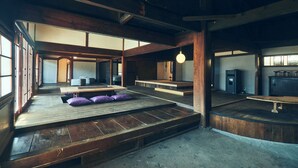 A spacious room with a wooden floor, a raised platform with cushions, and a hanging light fixture. - Kominka Yado Loof Kyonoie (Hokuto)