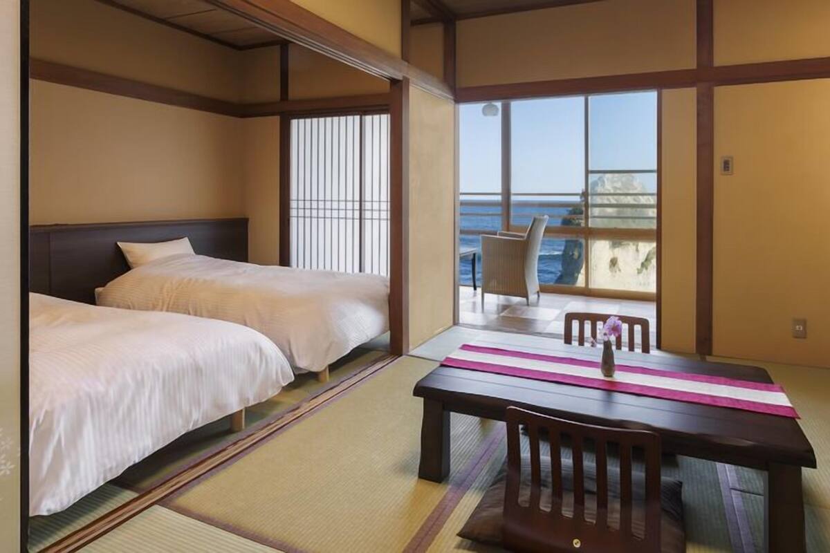 Una habitación japonesa tradicional con suelo de tatami, dos camas, una mesa con un florero y vista al mar.