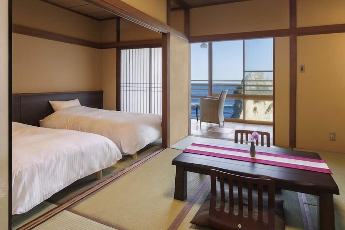 Una habitación japonesa tradicional con suelo de tatami, dos camas, una mesa con un florero y vista al mar.