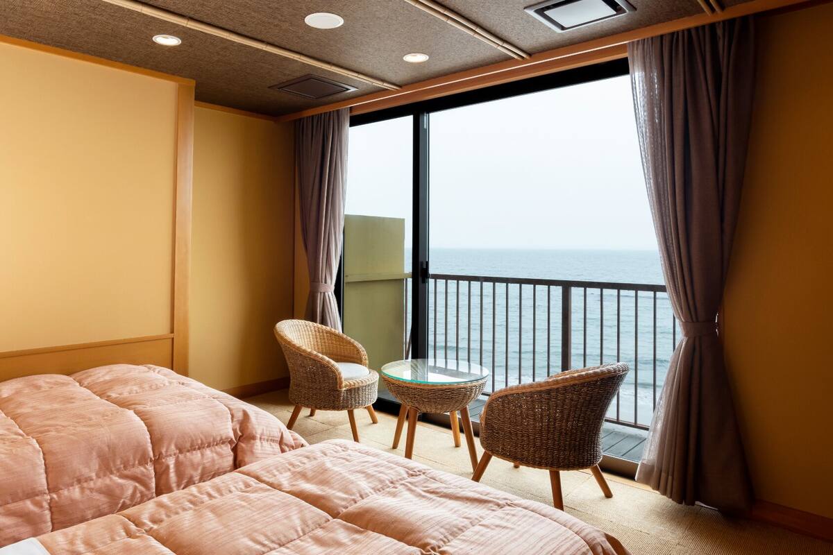 Habitación de hotel con cama, dos sillones de mimbre, una mesita y balcón con vista al mar.