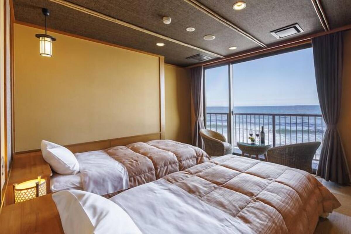 Habitación de hotel con una cama grande, una mesita con dos sillas y vista al océano.