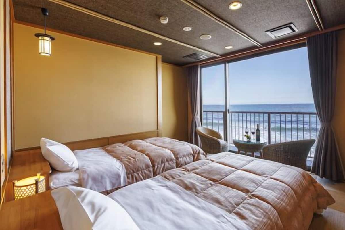 Habitación de hotel con una cama grande, una mesita con dos sillas y vista al océano.