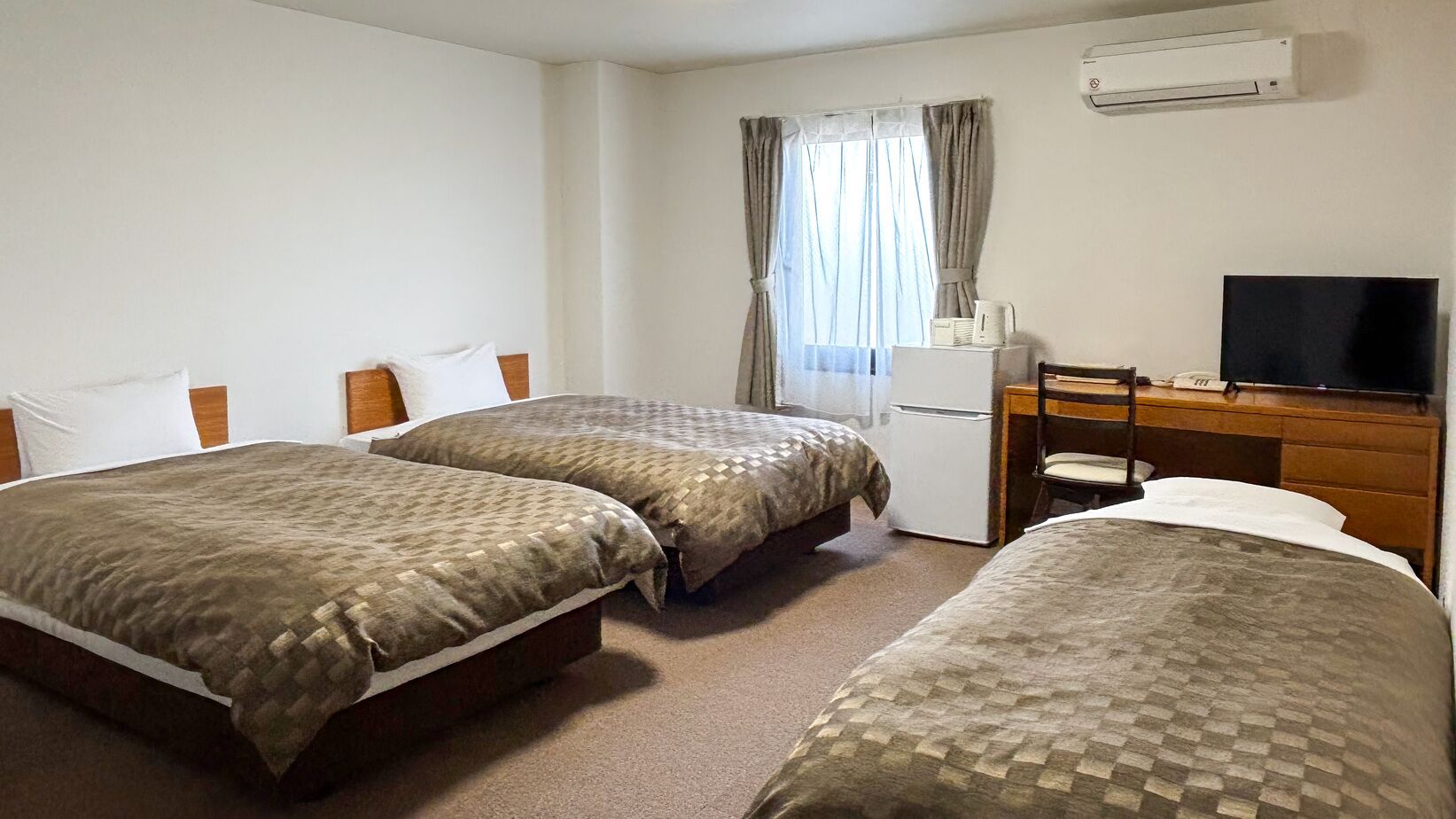 Habitación de hotel con dos camas, un escritorio, una silla, un televisor y un equipo de aire acondicionado.