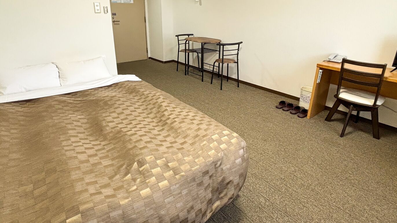 Una habitación de hotel con cama, escritorio, silla y una mesita.
