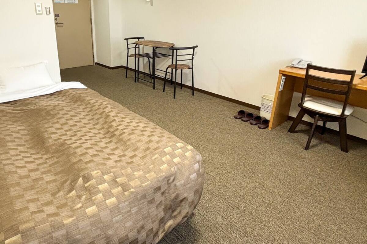 A hotel room with a bed, a desk, a chair, and a small table.