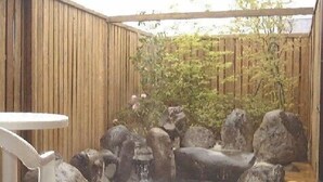 A wooden deck with a hot tub surrounded by rocks and a small waterfall feature. - Hiiragi Cottage (Hita)
