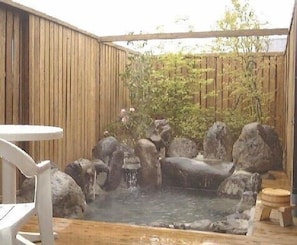 Una terraza de madera con un jacuzzi rodeado de rocas y una pequeña cascada.