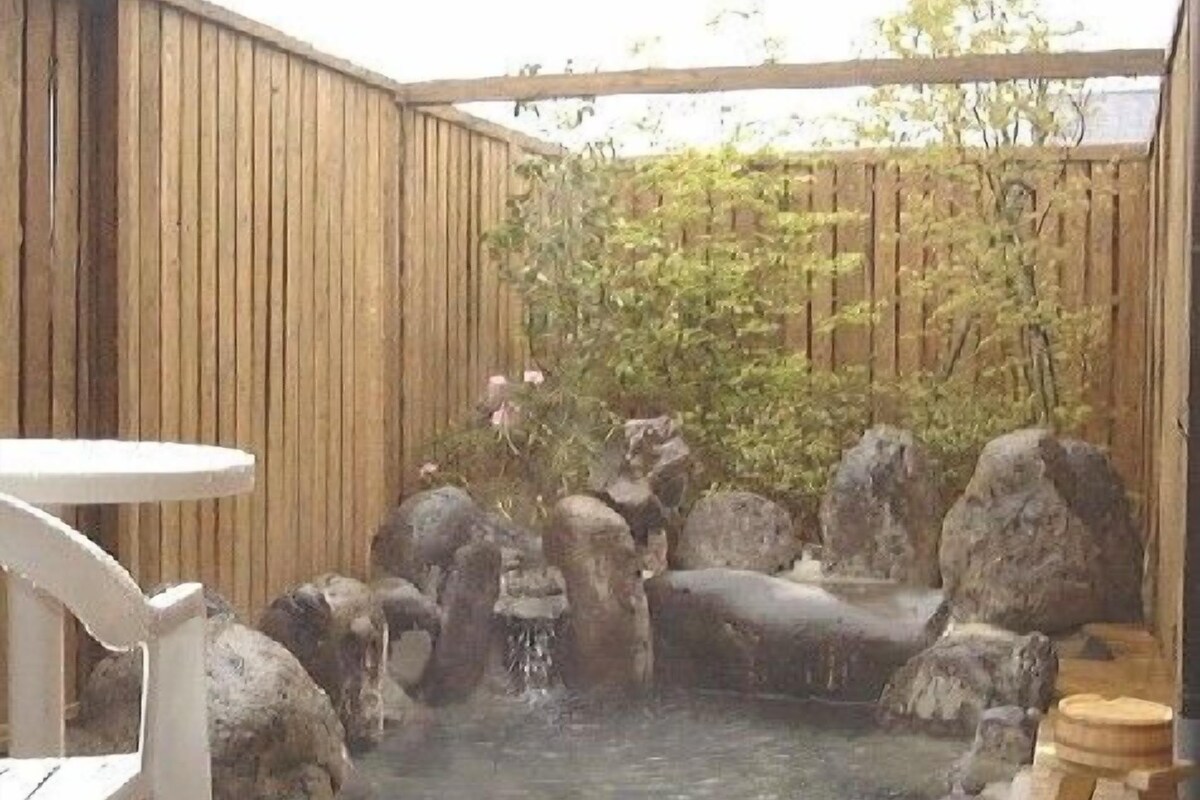 A wooden deck with a hot tub surrounded by rocks and a small waterfall feature.