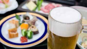 A glass of beer with a frothy head, a plate of assorted food items, and a blurred background.