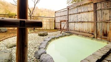 A traditional Japanese onsen with a stone bath surrounded by a wooden fence and a bamboo wall.