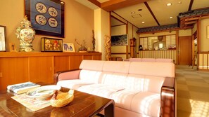 A traditional Japanese-style living room with a sofa, a wooden table with books and a basket, and various decorative items. - Nasuyumoto Onsen Ryokan Shimizuya (Nasu)