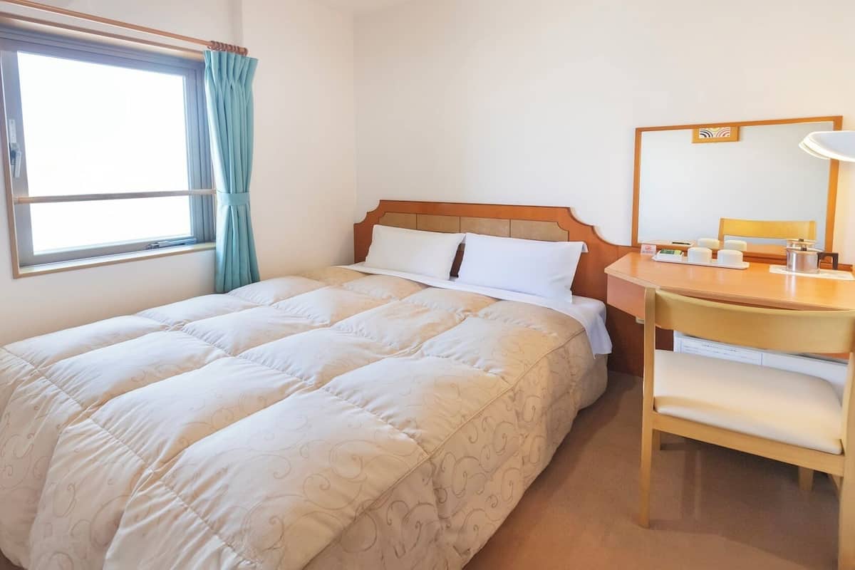 A hotel room with a bed, a desk, a chair, a television, and a window with curtains.