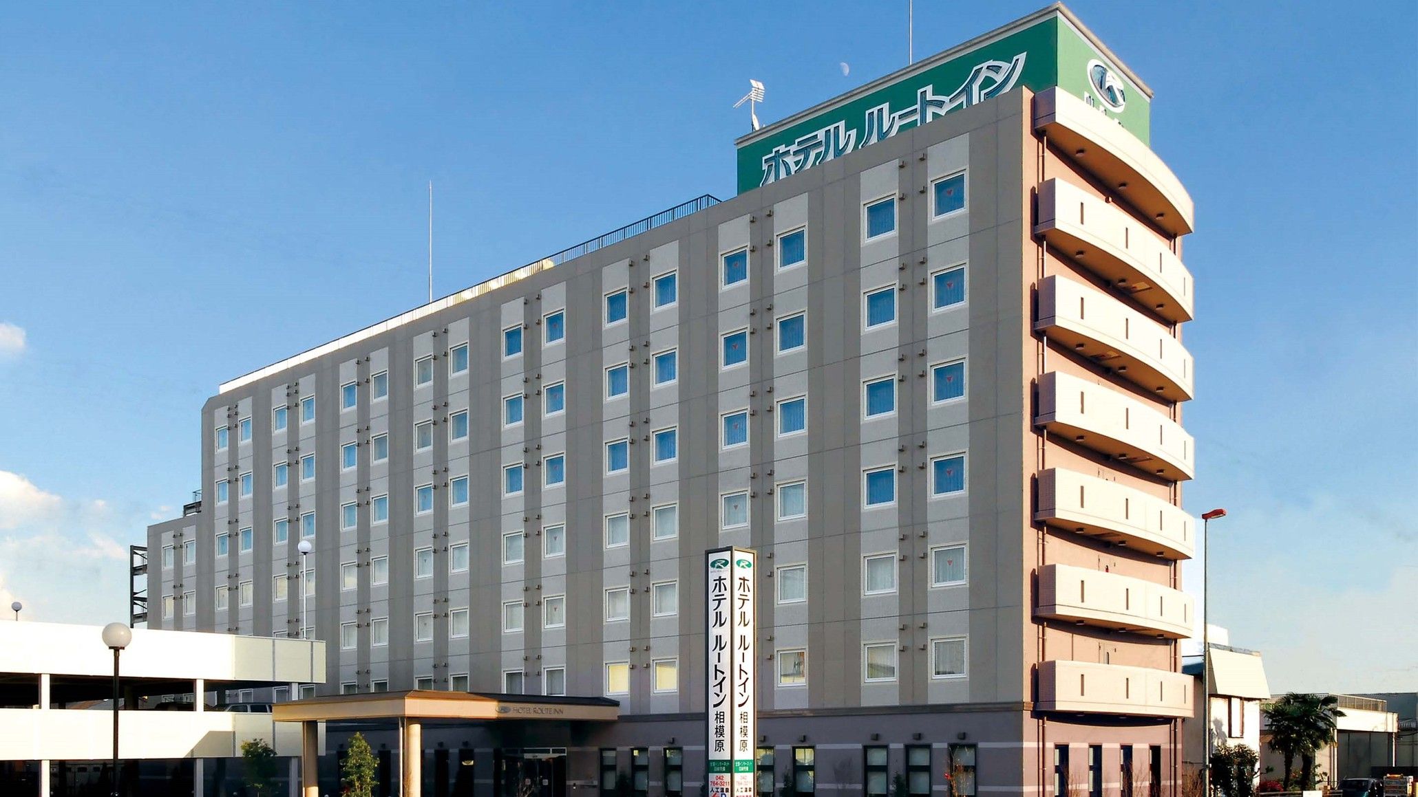 Ett hotell med flera våningar, ett stort, grönt skylt på taket, många fönster och en slät fasad.