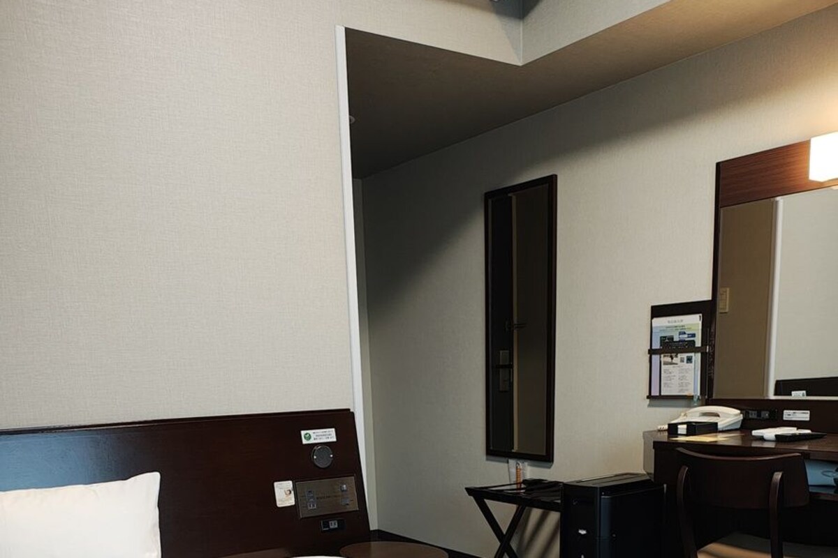 A hotel room with a large bed, a desk with a chair, a mirror, and a small table.