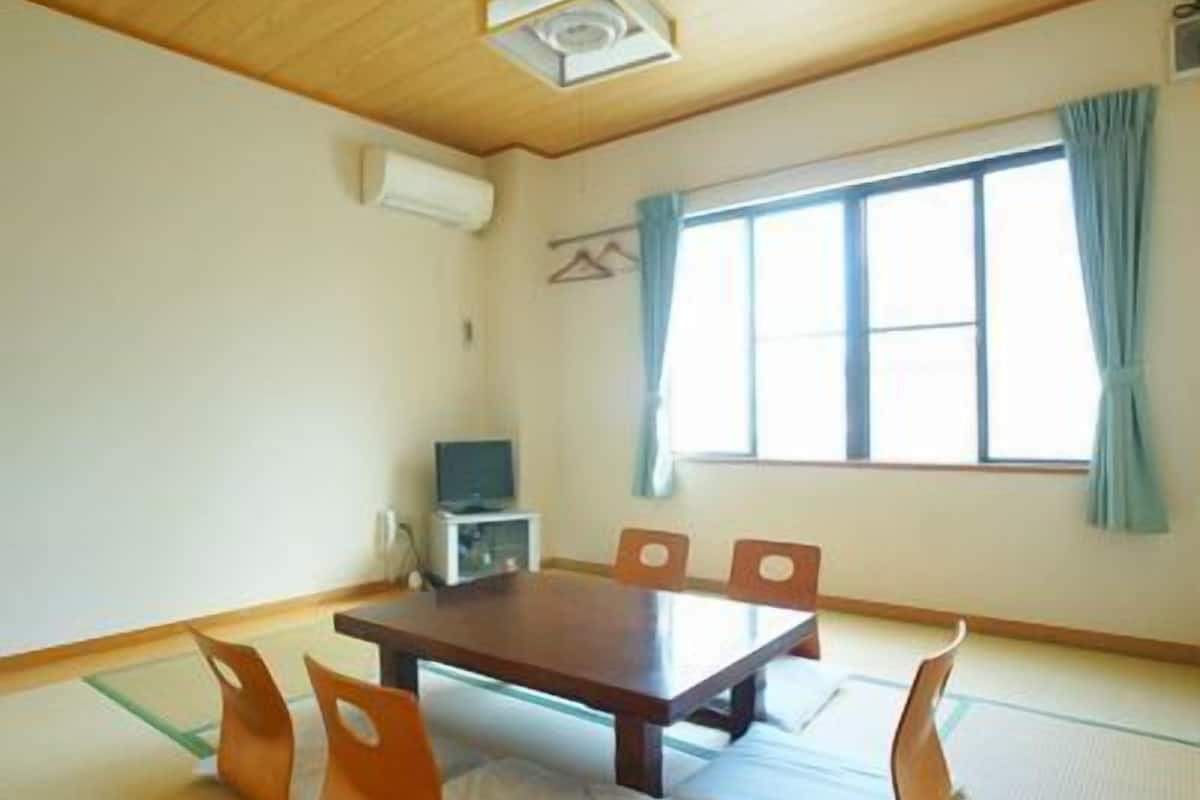 A room with tatami mats, a wooden table, chairs, a television, and a window with curtains.