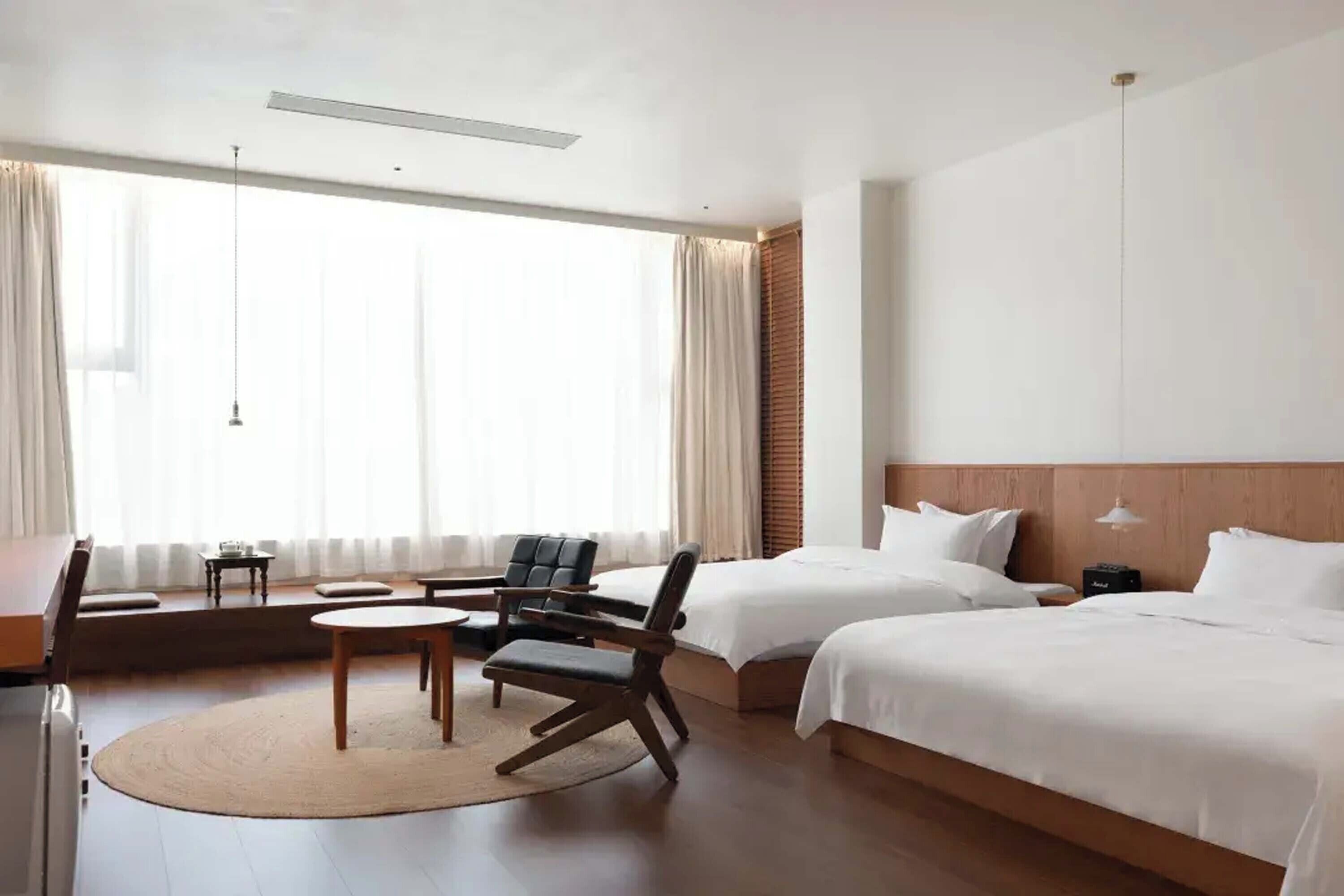 Een hotelkamer met twee bedden, een bureau, een stoel en een groot raam met gordijnen.