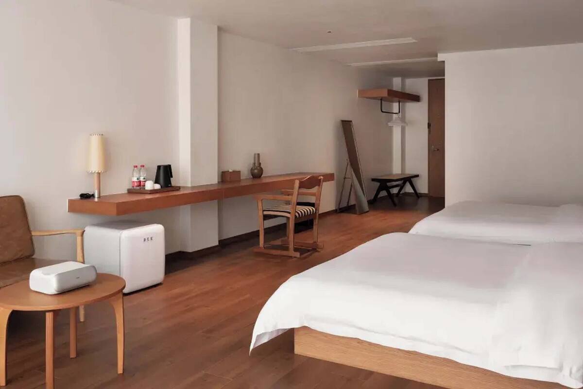 Ett hotellrum med en säng, ett skrivbord, en stol, en lampa och ett litet bord.