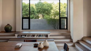 Een modern interieur met een groot raam, boekenkasten, een houten tafel en een vaas.