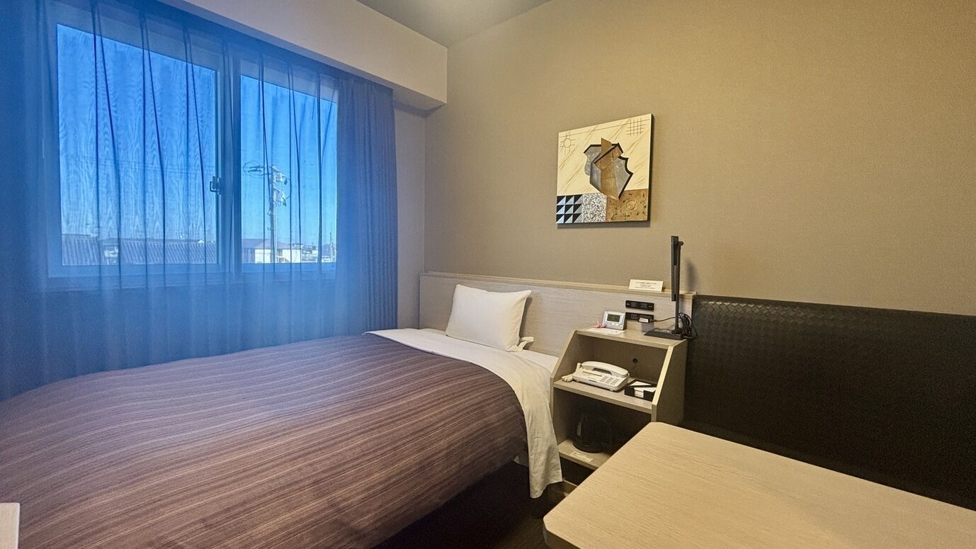 Quarto de hotel com cama, escrivaninha, telefone e um quadro na parede.