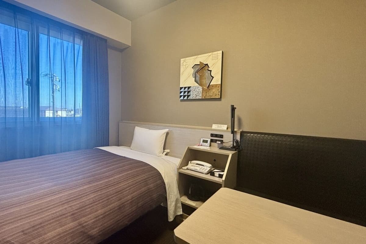 A hotel room with a bed, a desk, a telephone, and a painting on the wall.