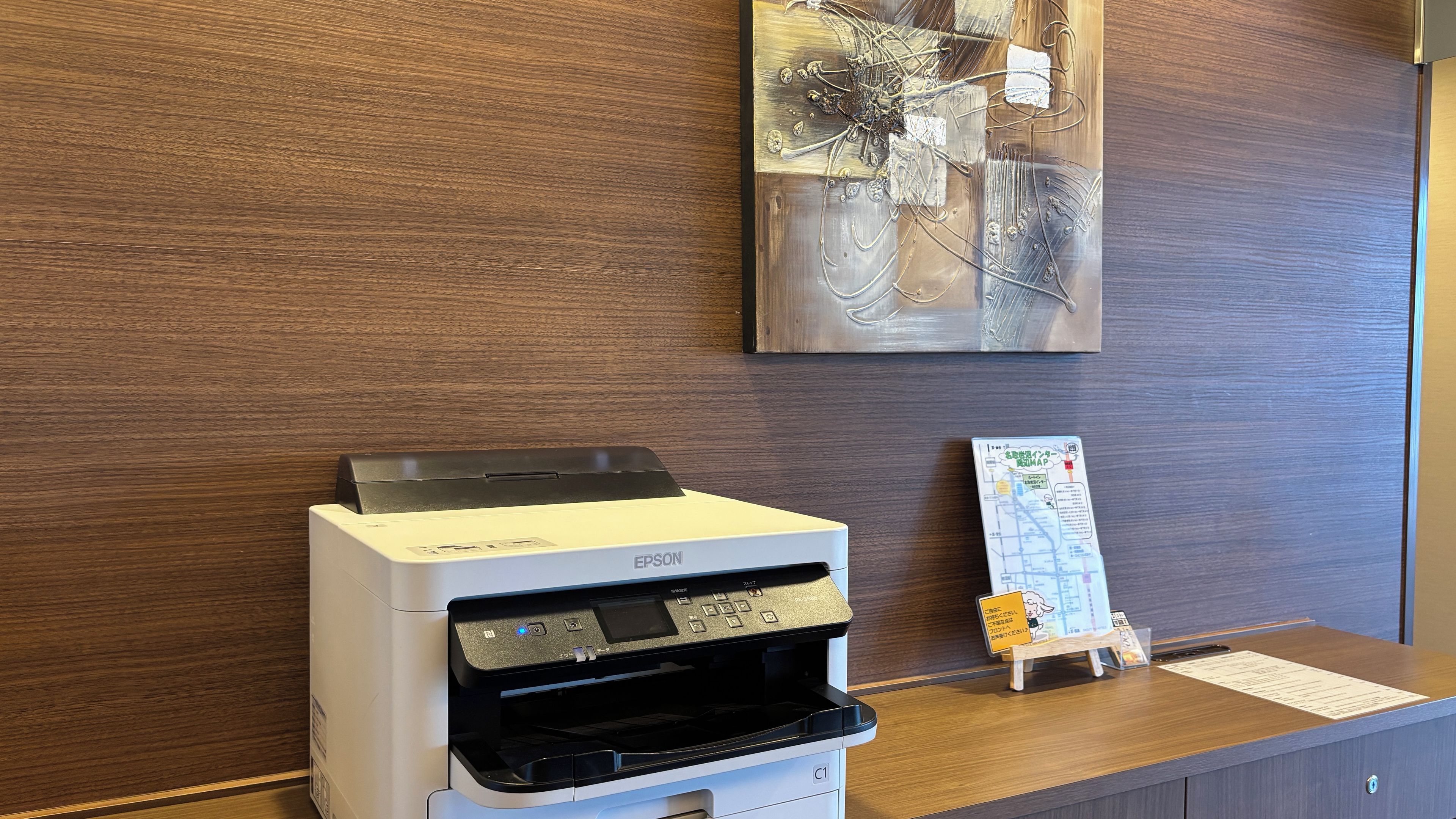 A reception desk with a printer, a map stand, and a wall-mounted abstract art piece.