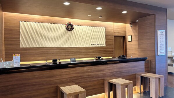 A hotel reception desk with a wooden finish, a digital clock, and a menu board. - Hotel Route-inn Natori Iwanuma Inter (Iwanuma)