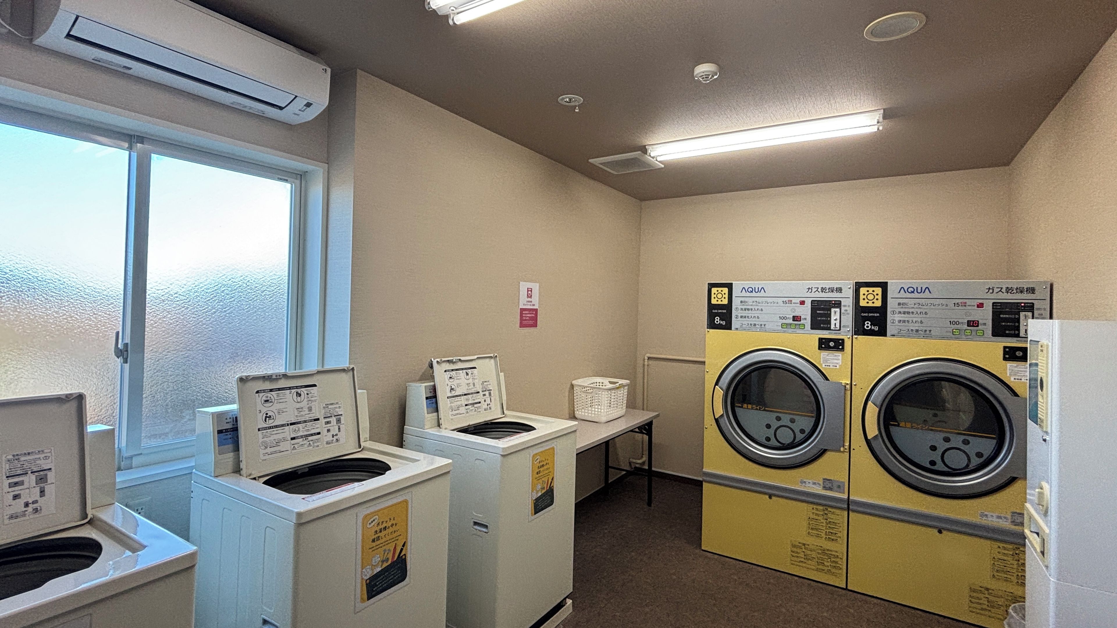 A laundry room with two front-loading washing machines, a dryer, and an air conditioning unit.