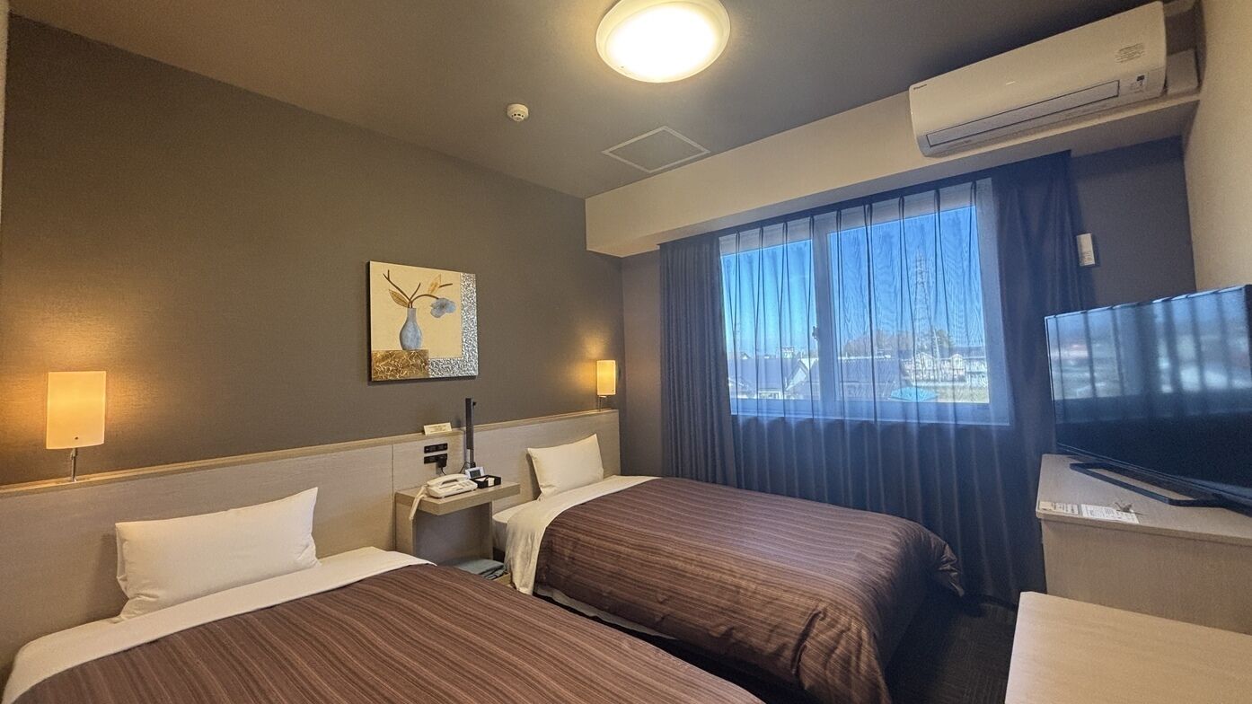 Quarto de hotel com duas camas, uma escrivaninha com telefone, televisão de tela plana e um quadro na parede.