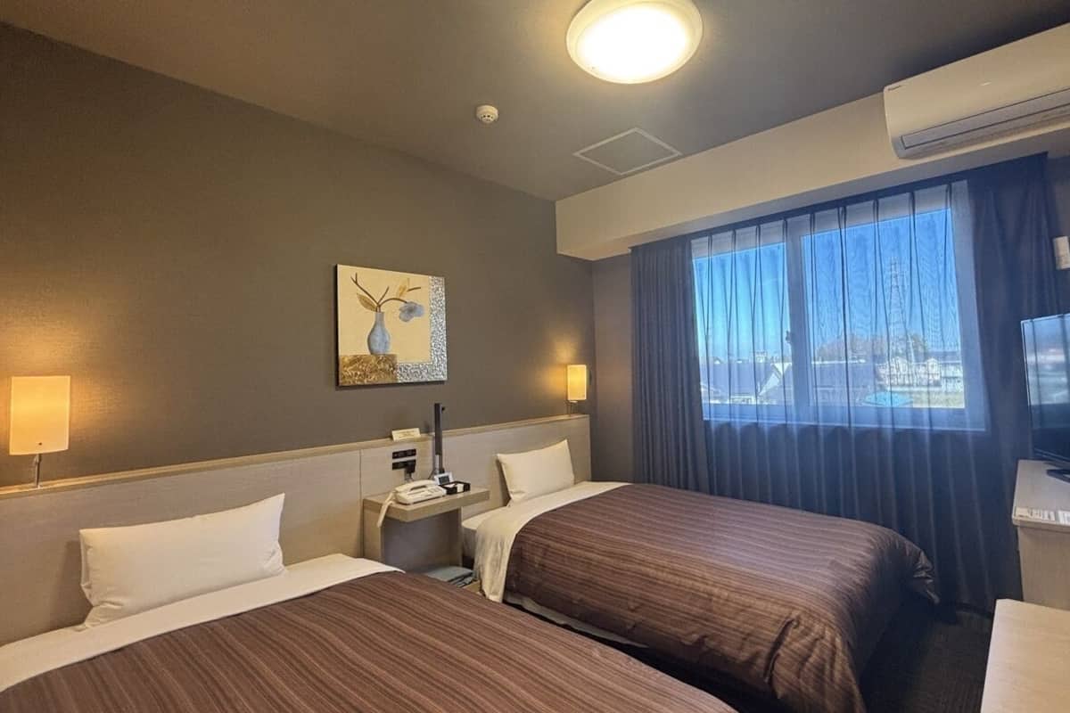 A hotel room with two beds, a desk with a telephone, a flat-screen TV, and a painting on the wall.