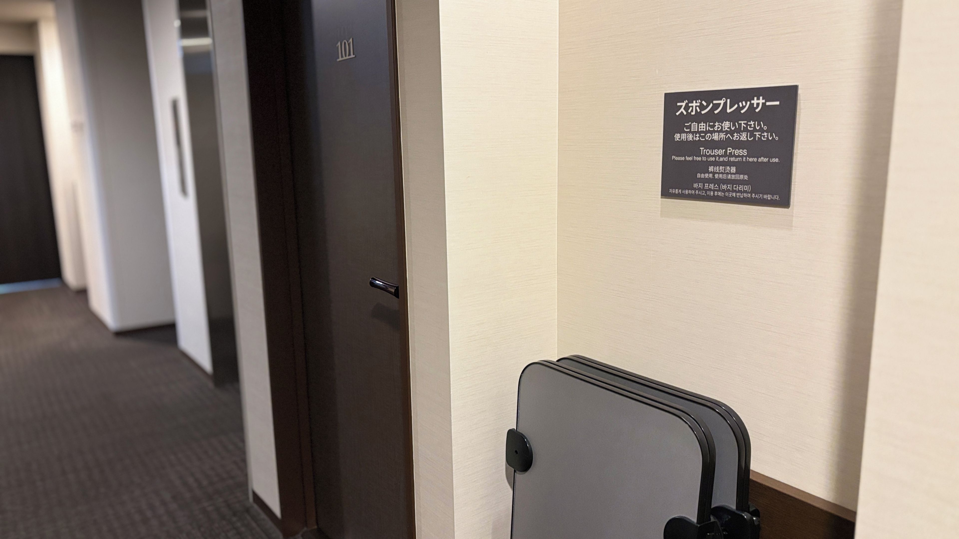 A hotel room with a door marked with the number 101, a sign with instructions in Japanese, and a suitcase against the wall.