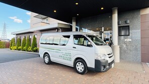 A white van parked in front of a hotel entrance with a modern design, a clear sky, and a visible power line tower in the background. - Hotel Route-inn Natori Iwanuma Inter (Iwanuma)