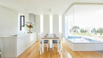 A modern kitchen with a dining area, wooden flooring, and a view of a swimming pool.