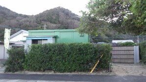 A building with a green exterior, a wooden fence, and a bush in front. - Seaside House (Uken)