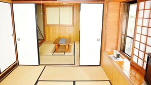 Ein traditioneller japanischer Raum mit Tatami-Bodenbelag, einem niedrigen Holztisch, Schiebetüren und einem Fenster mit Shoji-Bildschirmen.