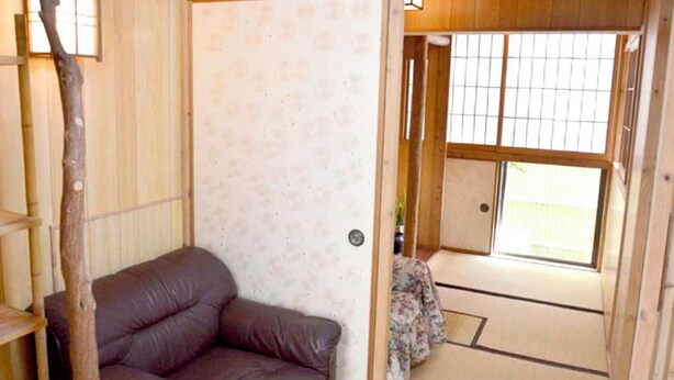 Ein traditioneller japanischer Raum mit Tatami-Bodenbelag, einer niedrigen Holztür und Blick ins Freie durch eine Schiebetür.