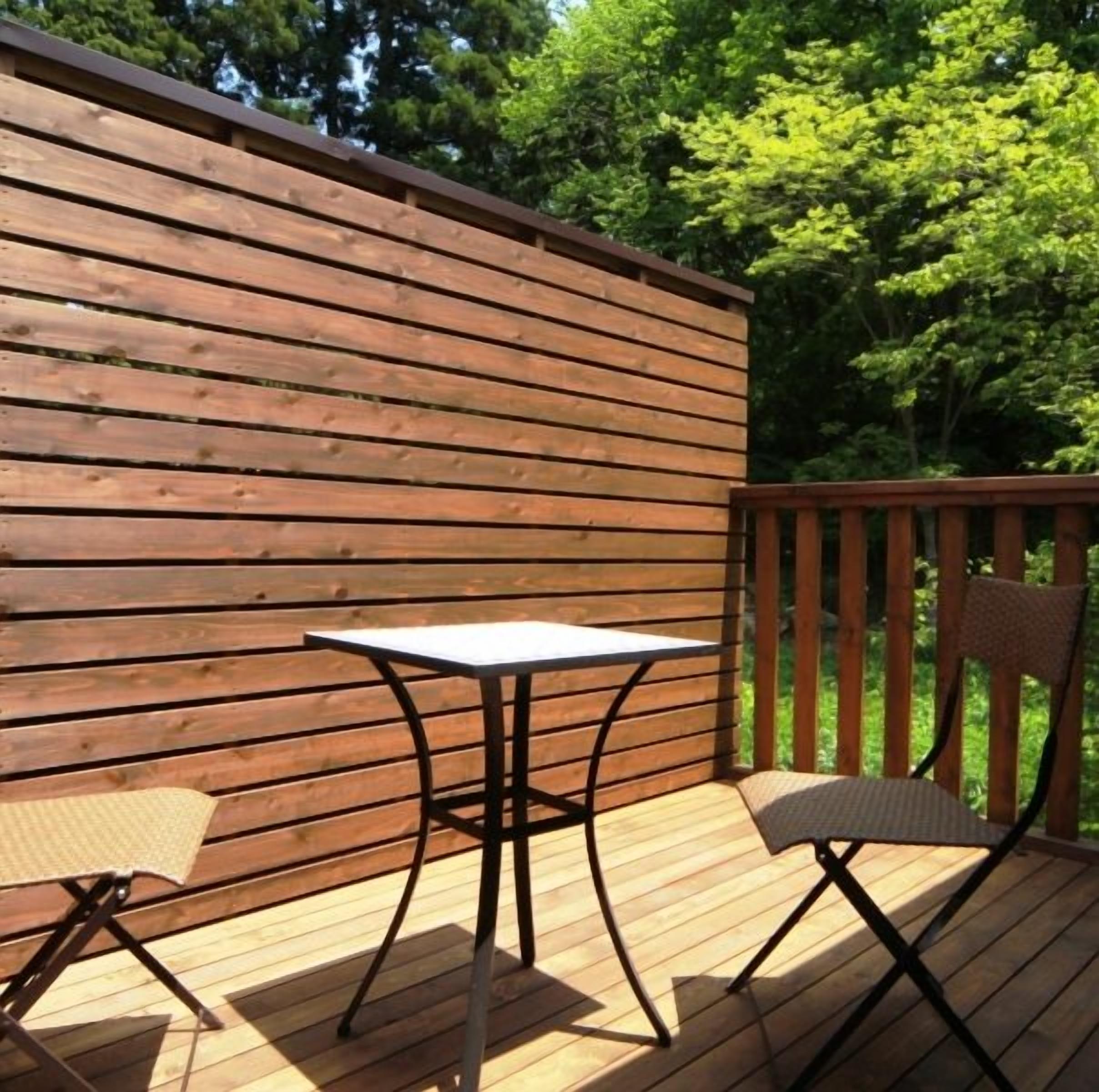 Una terraza exterior de madera con una mesa y sillas, rodeada por una valla de madera y árboles.