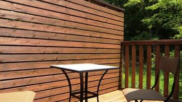 Una terraza exterior de madera con una mesa y sillas, rodeada por una valla de madera y árboles.