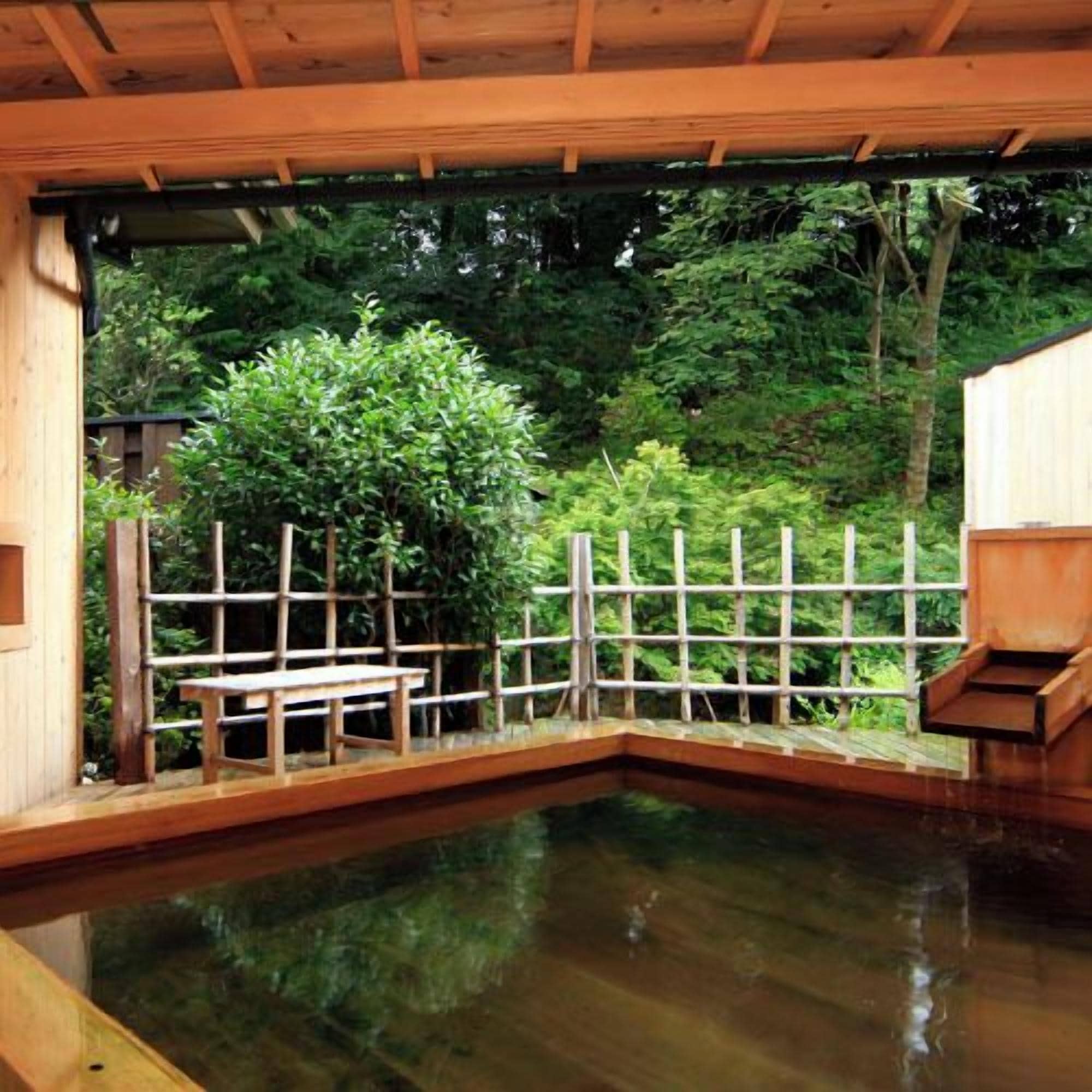Una estructura de madera con piscina, rodeada por una valla de madera y follaje.