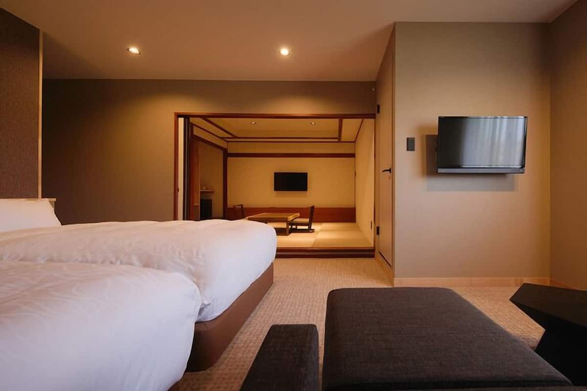 A hotel room with two beds, a TV mounted on the wall, a small table, and a bench.