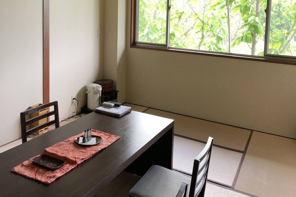 A traditional Japanese room with tatami flooring, a low table, and a window with a view of greenery.