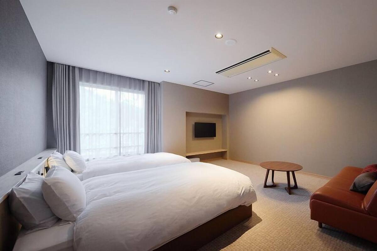 A hotel room with a large bed, a small sofa, a TV, and a ceiling air vent.