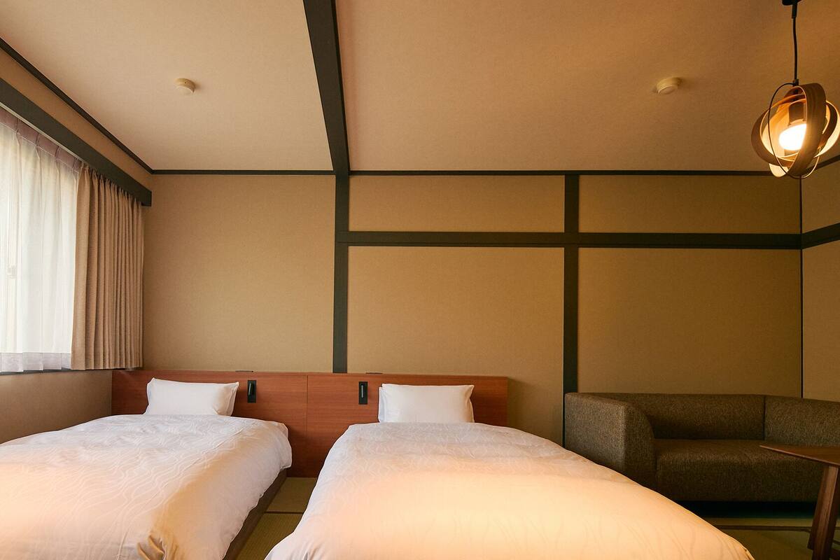 A hotel room with two beds, a sofa, a desk, and a hanging light fixture.