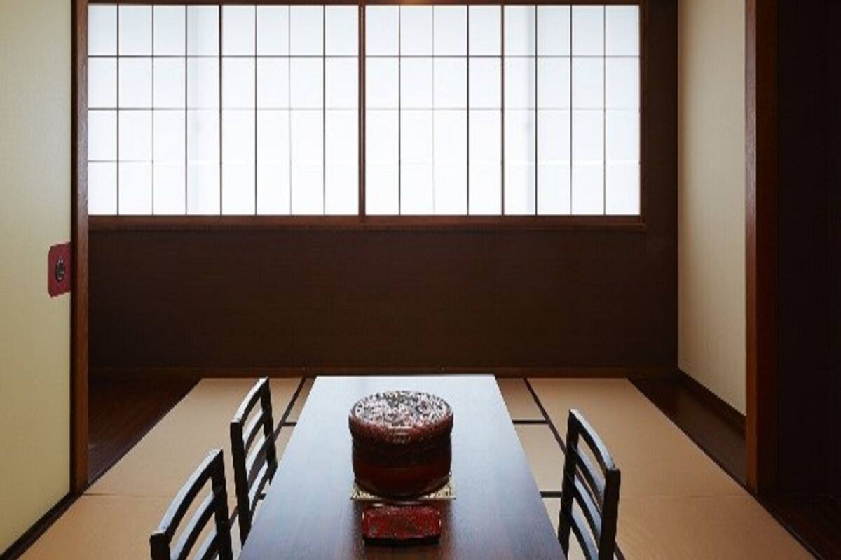 A traditional Japanese room with tatami flooring, a low table with a cake, and a large window with sliding doors.